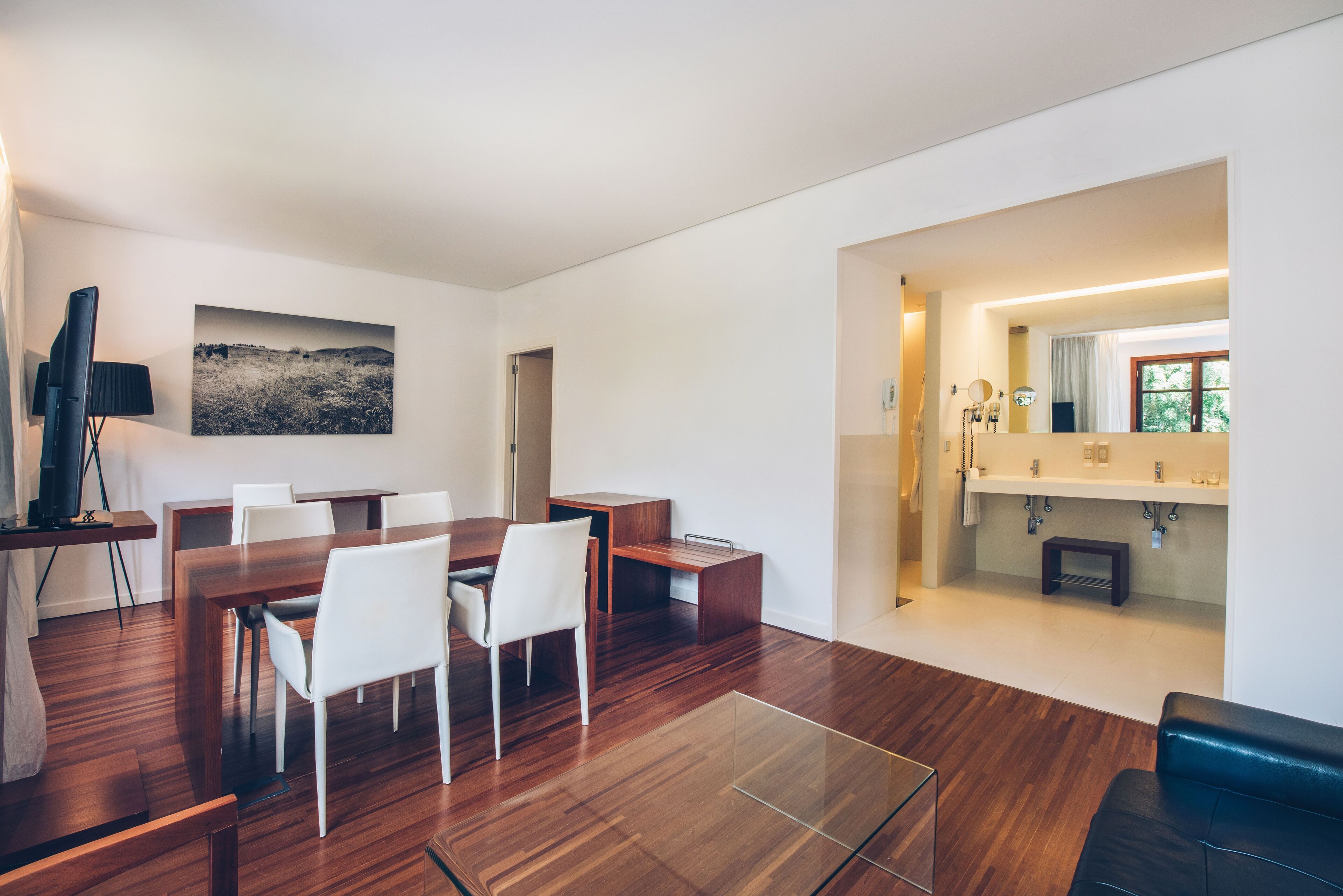 A modern living room with a wooden dining table, white chairs, a glass coffee table, and a black leather sofa.
