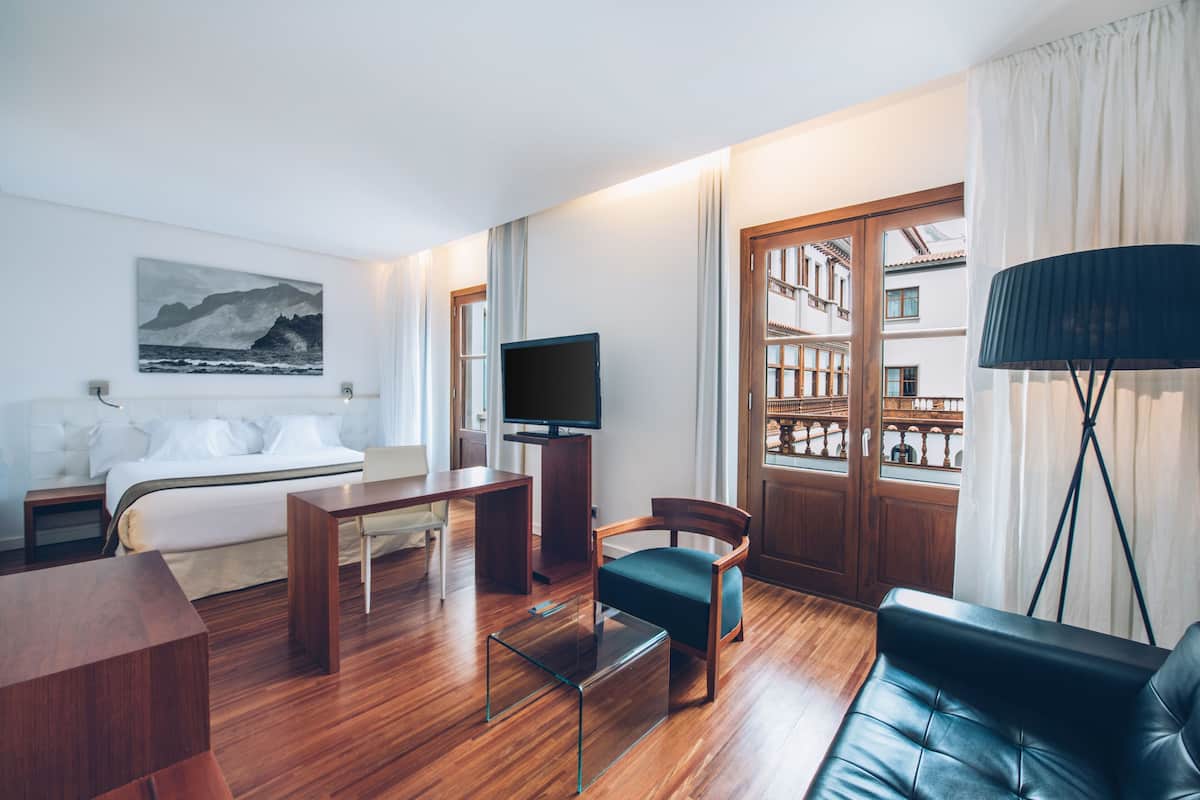 A modern hotel room with a bed, a desk, a chair, a TV, and a bookshelf.