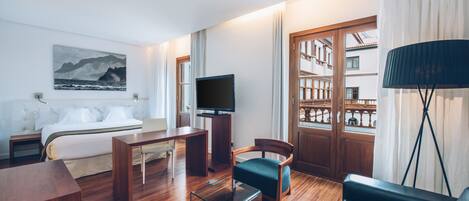 A modern hotel room with a bed, a desk, a chair, a TV, and a bookshelf.