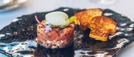 A black plate with a dish of raw fish, a scoop of ice cream, and toasted bread.