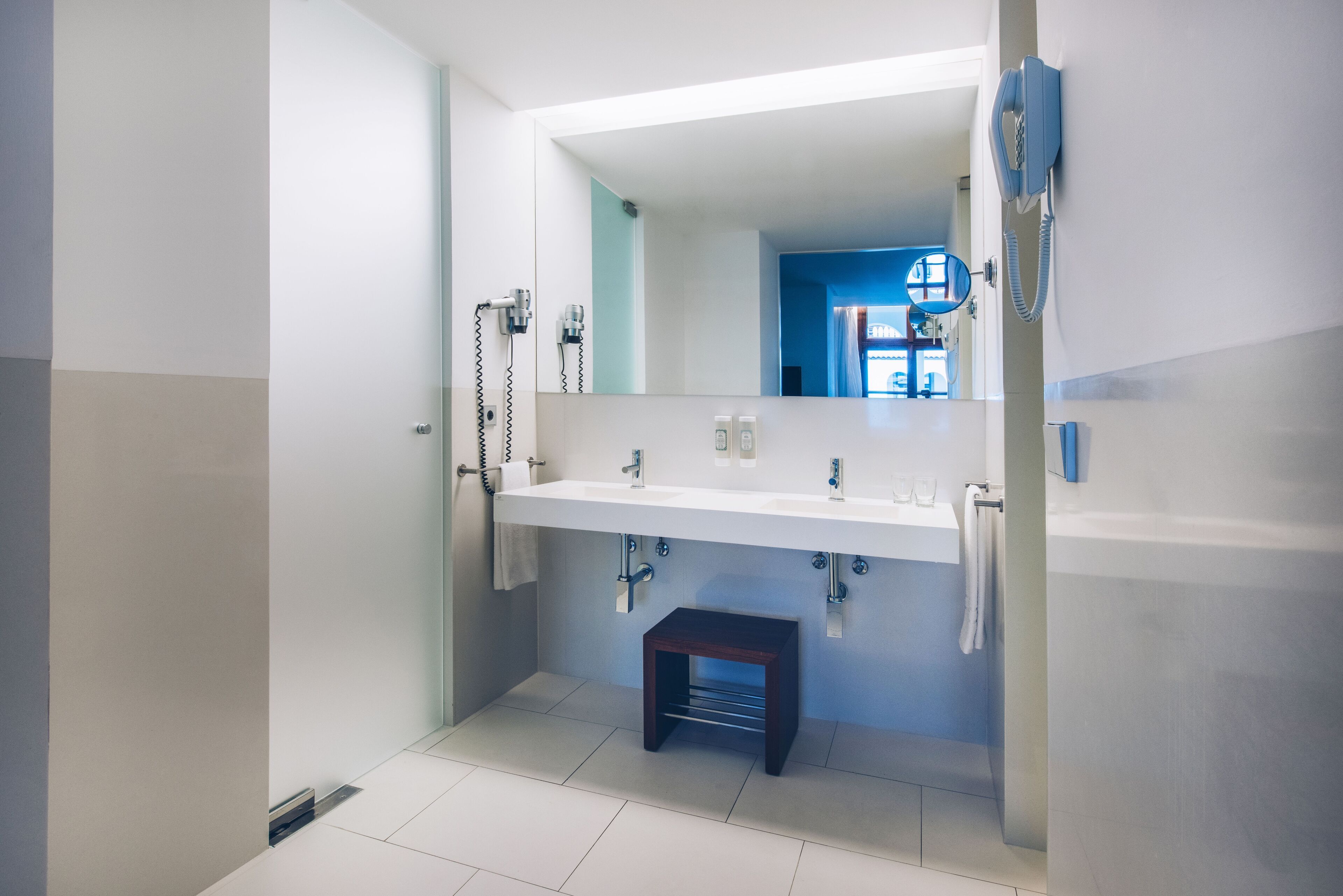 Un baño moderno con un espejo grande, lavamanos blanco y un taburete pequeño.