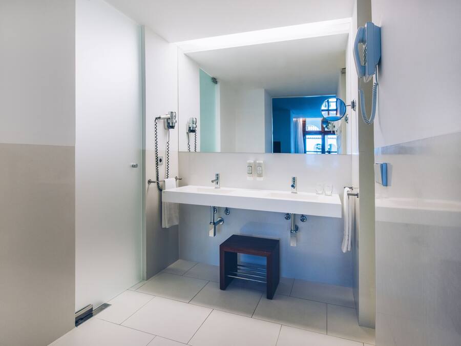 Un baño moderno con un espejo grande, lavamanos blanco y un taburete pequeño.
