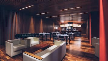 A modern restaurant with wooden flooring, white sofas, and a central dining area with tables and chairs.