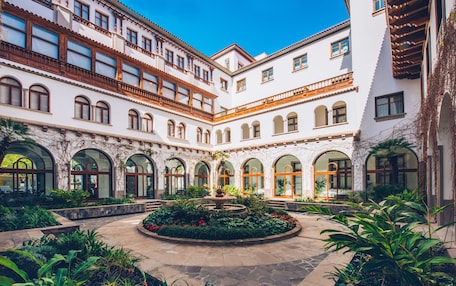 A courtyard with a fountain, surrounded by arched windows and a white building with wooden balconies.