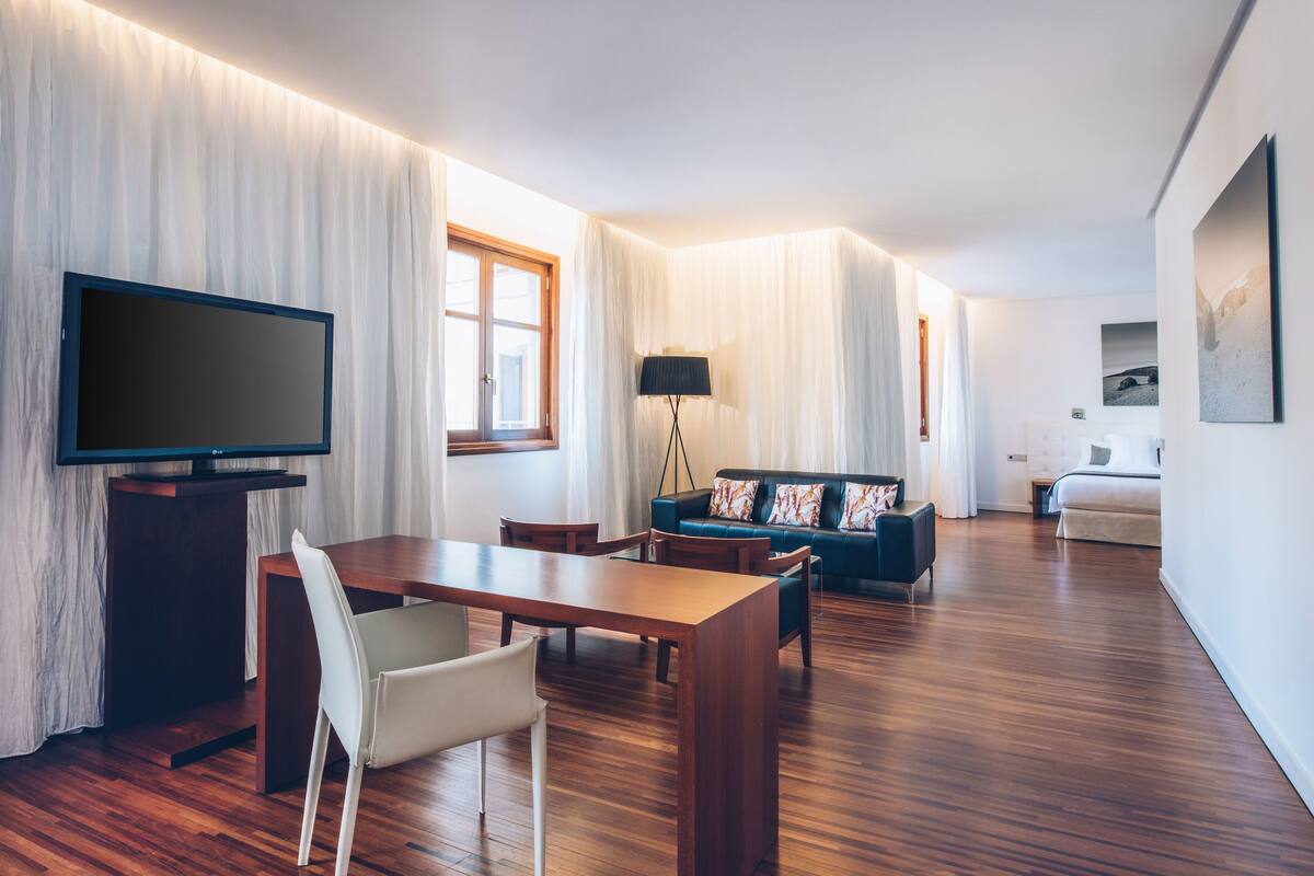 A modern living room with a wooden floor, a TV, a sofa, and a dining area.