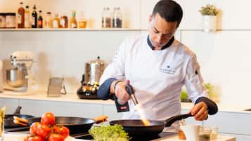 Un chef, vêtu d’un uniforme blanc, cuisine à l’aide d’une poêle sur une cuisinière.