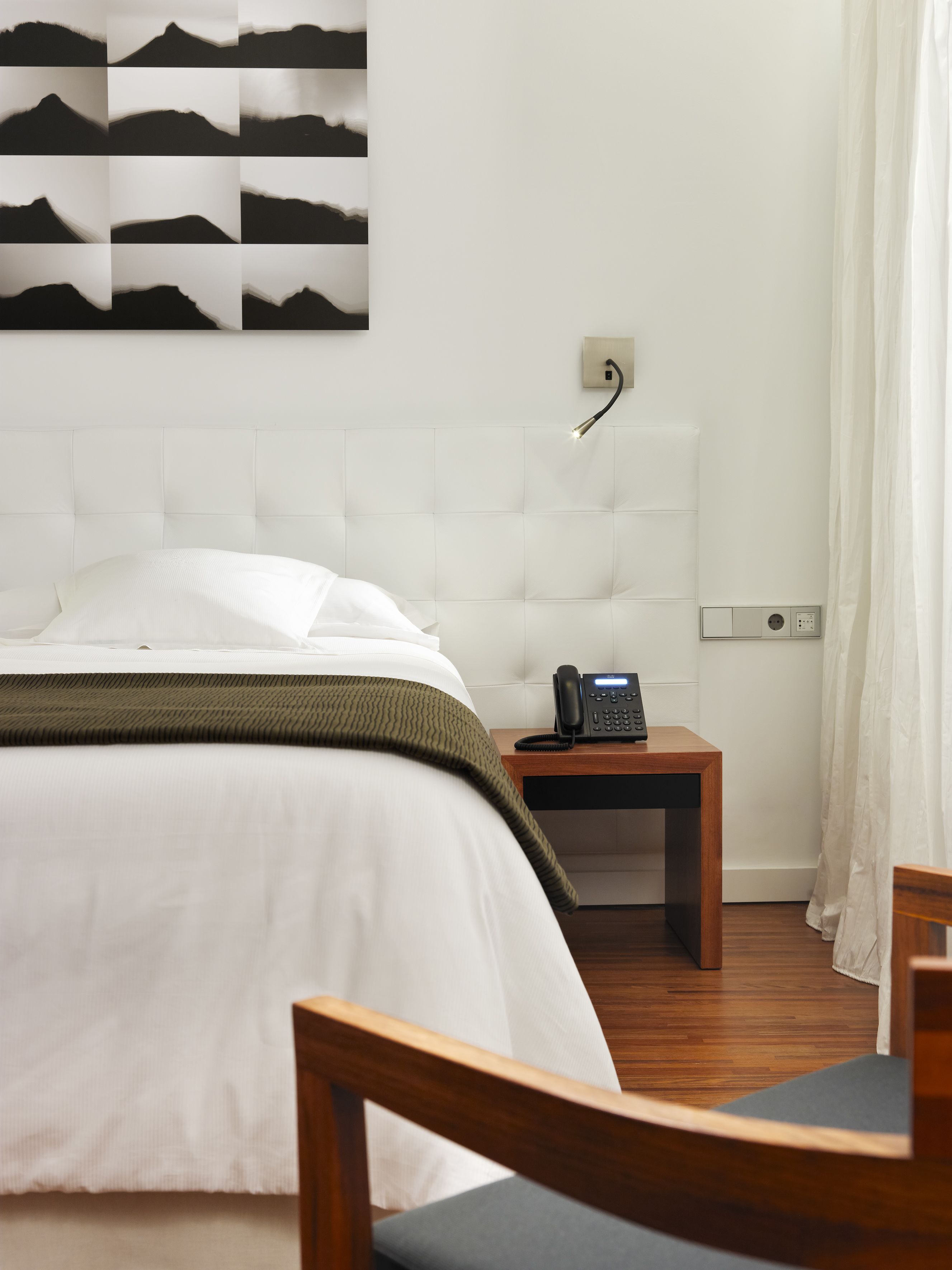 A hotel room with a large bed, a bedside table with a phone, a wooden nightstand, and a chair.