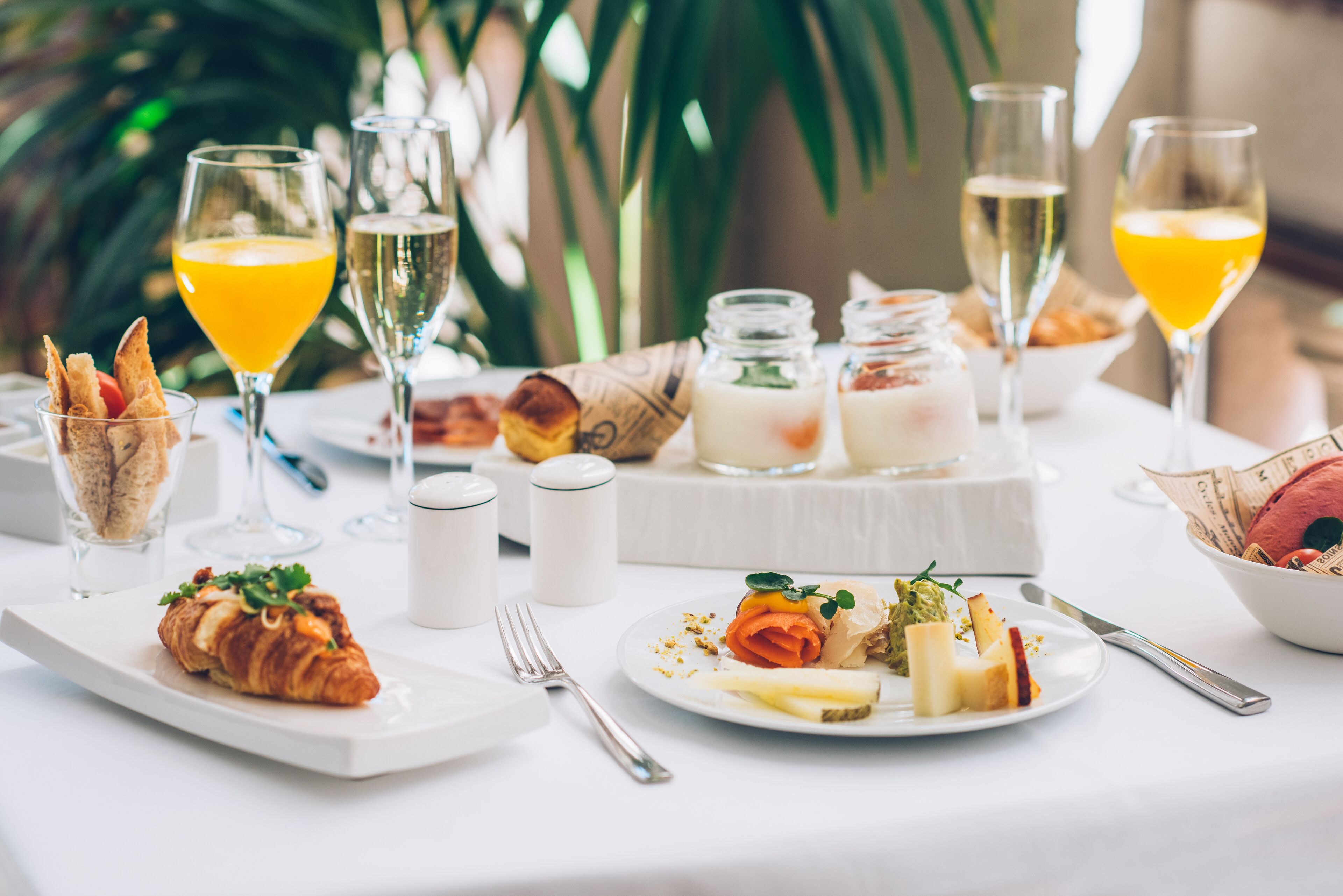 Una mesa dispuesta con croissants, queso y fruta, junto a vasos de zumo de naranja y champán.