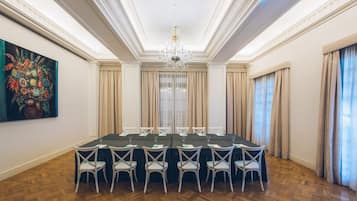 Un salón de conferencias con una larga mesa, sillas blancas y una araña.