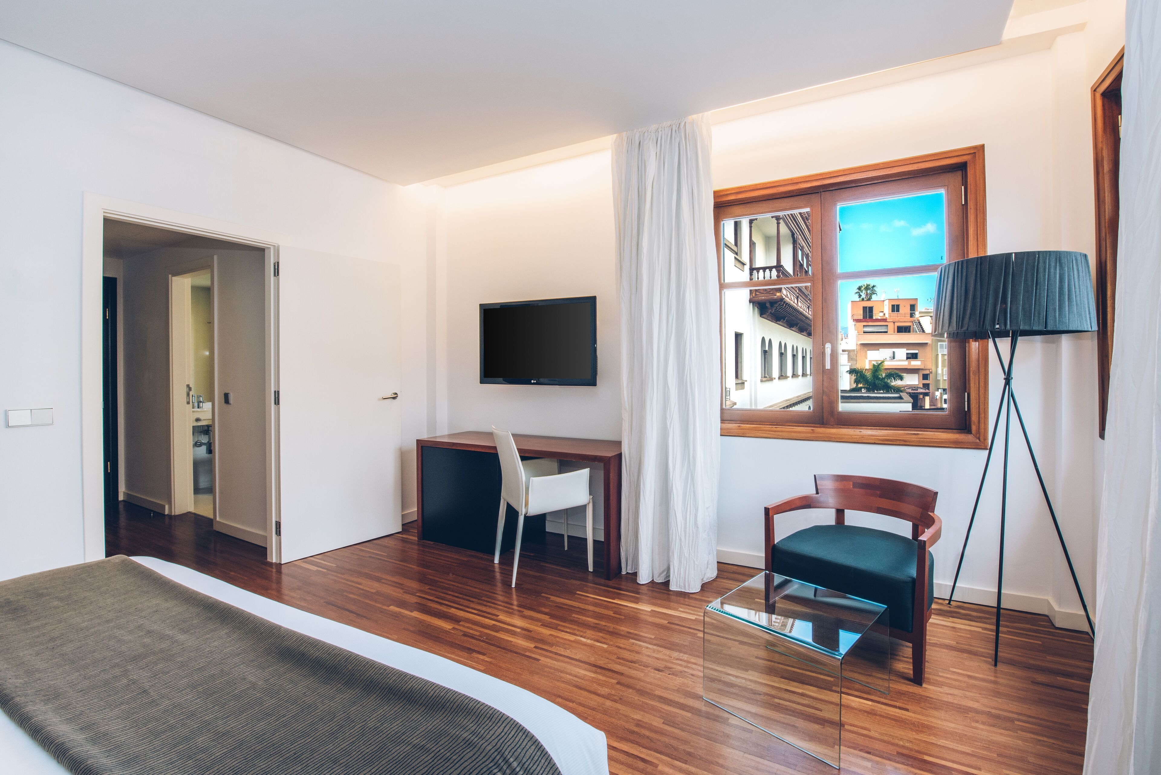 A hotel room with a bed, a desk, a chair, a TV, and a window with a view of buildings.