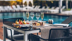A dining table with a meal, glasses of white wine, and a poolside setting with lounge chairs and umbrellas in the background. - Iberostar Heritage Grand Mencey (Santa Cruz de Tenerife)