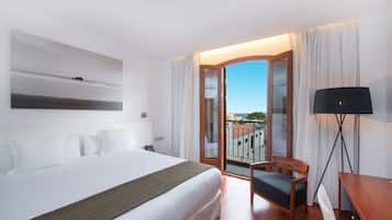 Habitación de hotel con una cama grande, una silla, un escritorio y vistas de la ciudad a través de un ventanal.