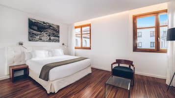 Ein modernes Hotelzimmer mit einem großen Bett, Holzboden, einem kleinen Tisch und einem Stuhl.