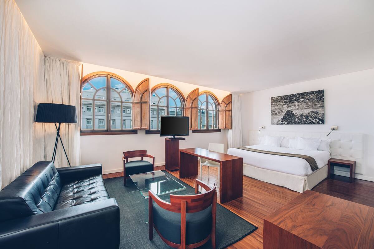 A modern hotel room with a large bed, a sofa, a desk, and a TV.