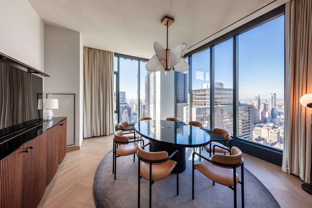 A modern conference room with a round table, chairs, and a city view through large windows.