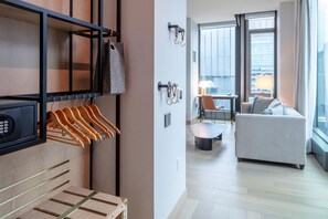 Une chambre d’hôtel dotée d’une armoire en bois, d’un coin salon avec un canapé et une table, et offrant une vue sur la ville grâce à de grandes fenêtres.