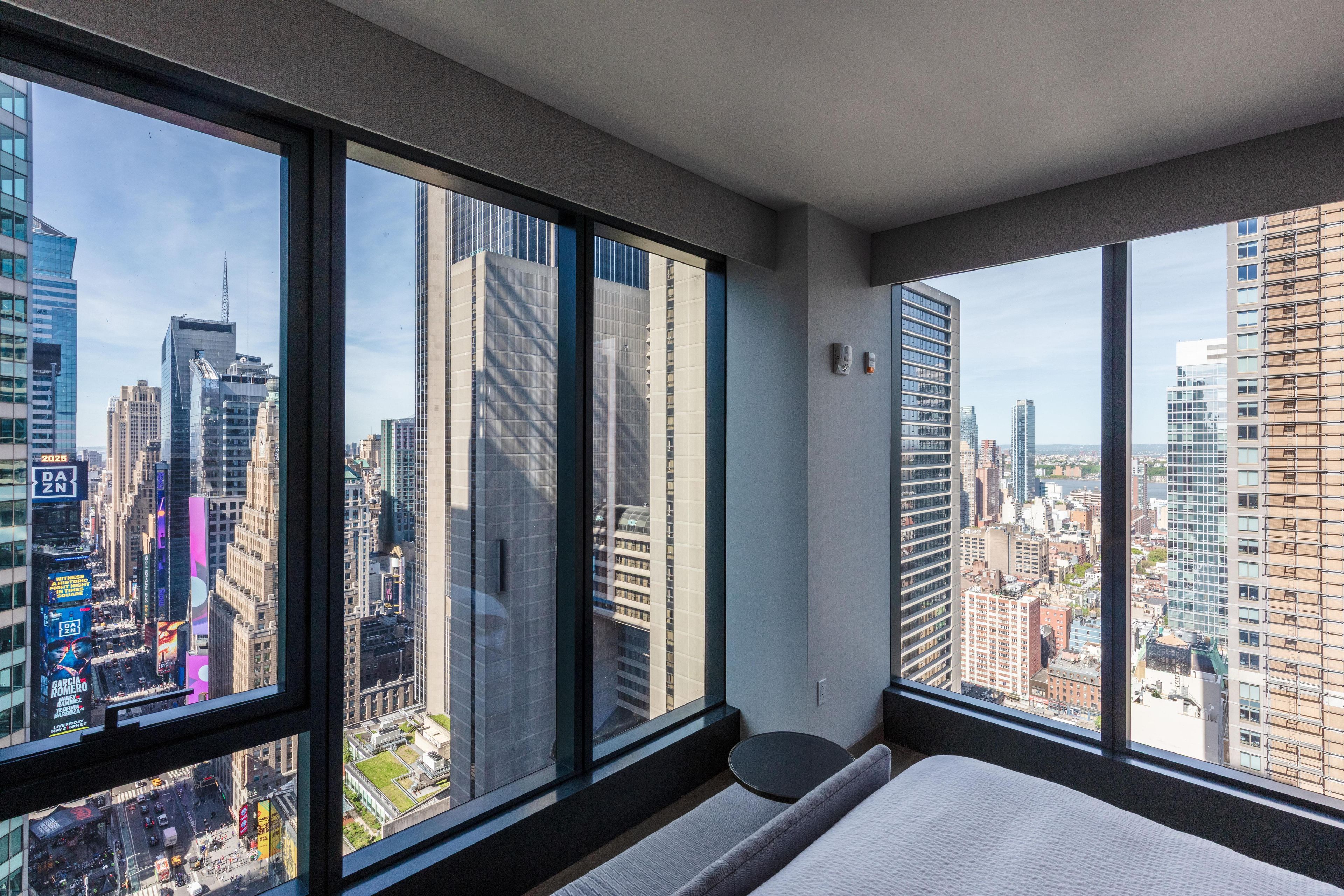 Habitación de hotel en un edificio alto, con ventanas amplias que ofrecen vistas a la ciudad.