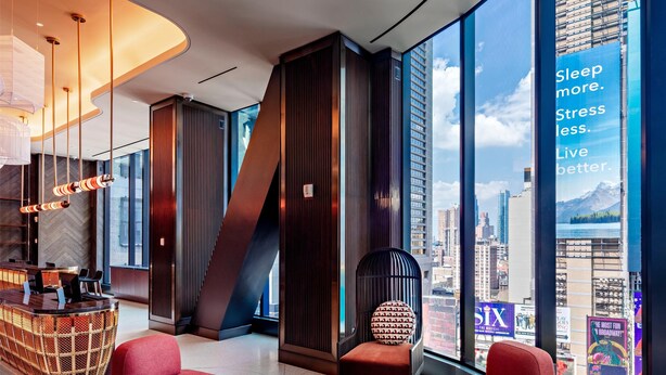 A modern hotel lobby with a curved ceiling, a reception desk, red seating, and large windows offering city views. - Tempo by Hilton New York Times Square (New York)