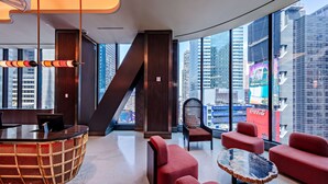 A modern lobby with a reception desk, red seating, a glass coffee table, and large windows offering city views. - Tempo by Hilton New York Times Square (New York)
