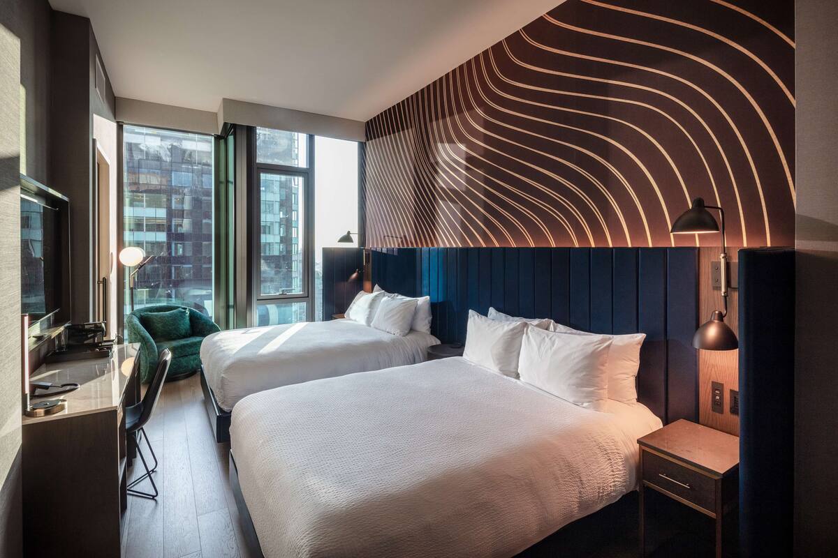 A hotel room with two beds, a desk, a chair, and a large window.