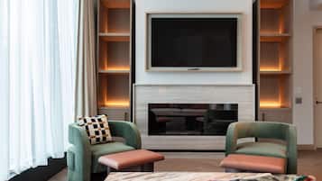 Una sala de estar moderna con un televisor de pantalla plana sobre la chimenea, sillones verdes y una alfombra estampada.