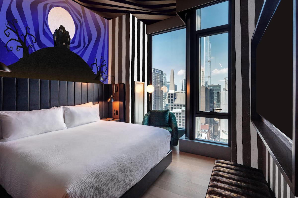 A modern hotel room with a large bed, a view of the cityscape, and a unique wall mural.