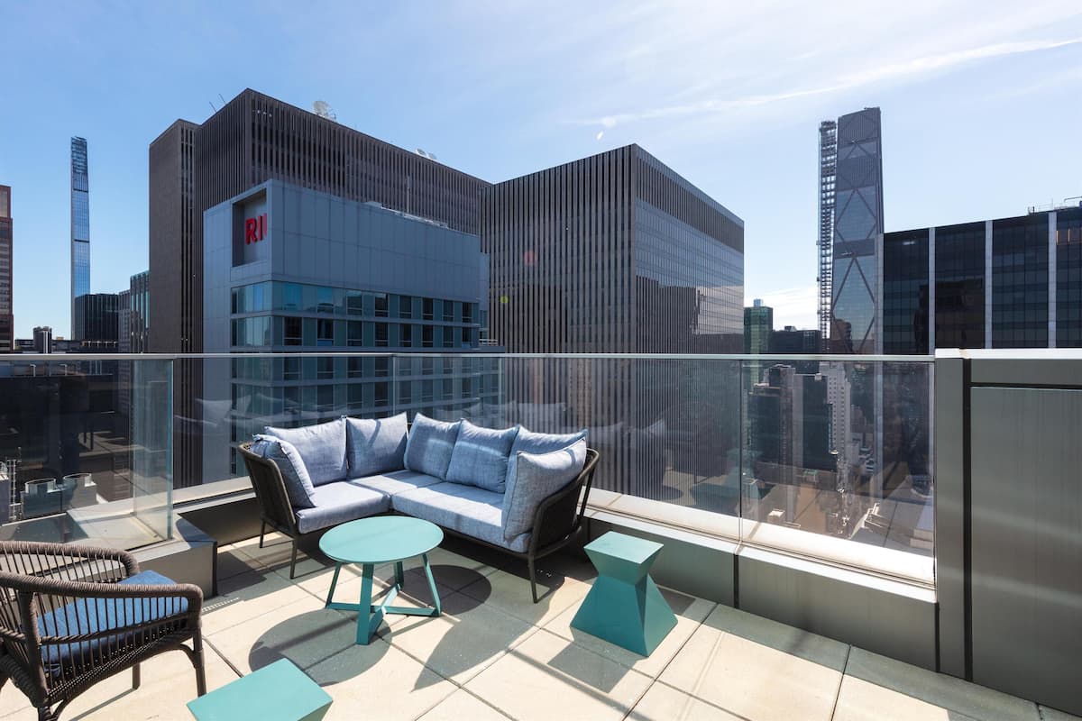 A rooftop terrace with a sofa, chairs, and tables, overlooking a cityscape with modern buildings.