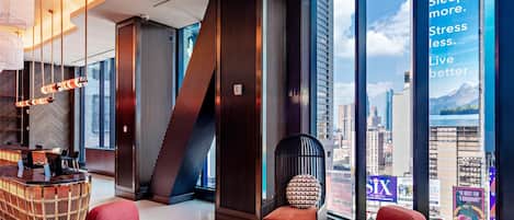 A modern hotel lobby with a curved ceiling, a reception desk, red seating, and large windows offering city views.