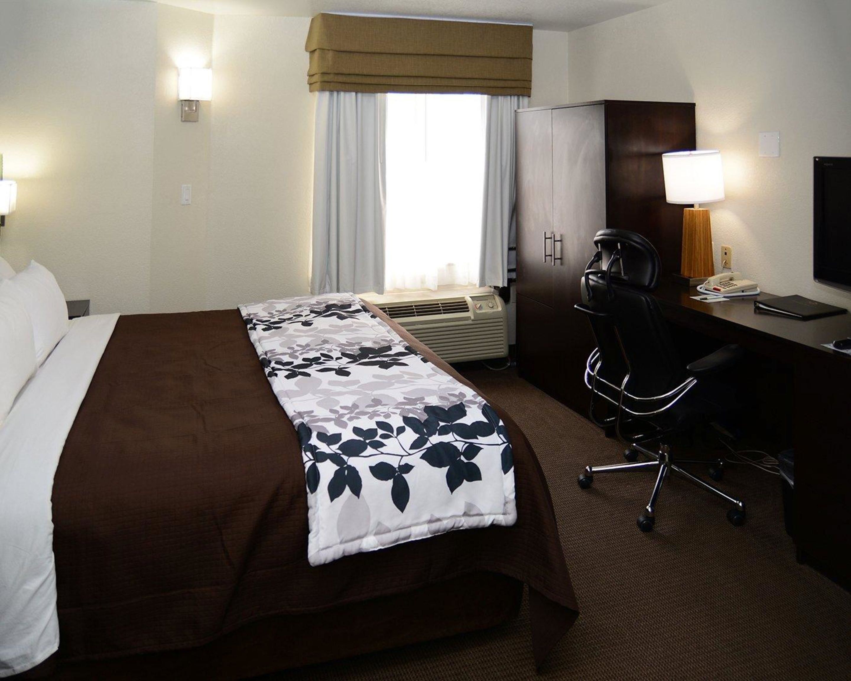 Ein Hotelzimmer mit Bett, Schreibtisch, Stuhl, Fernseher und einem Fenster mit Vorhängen.