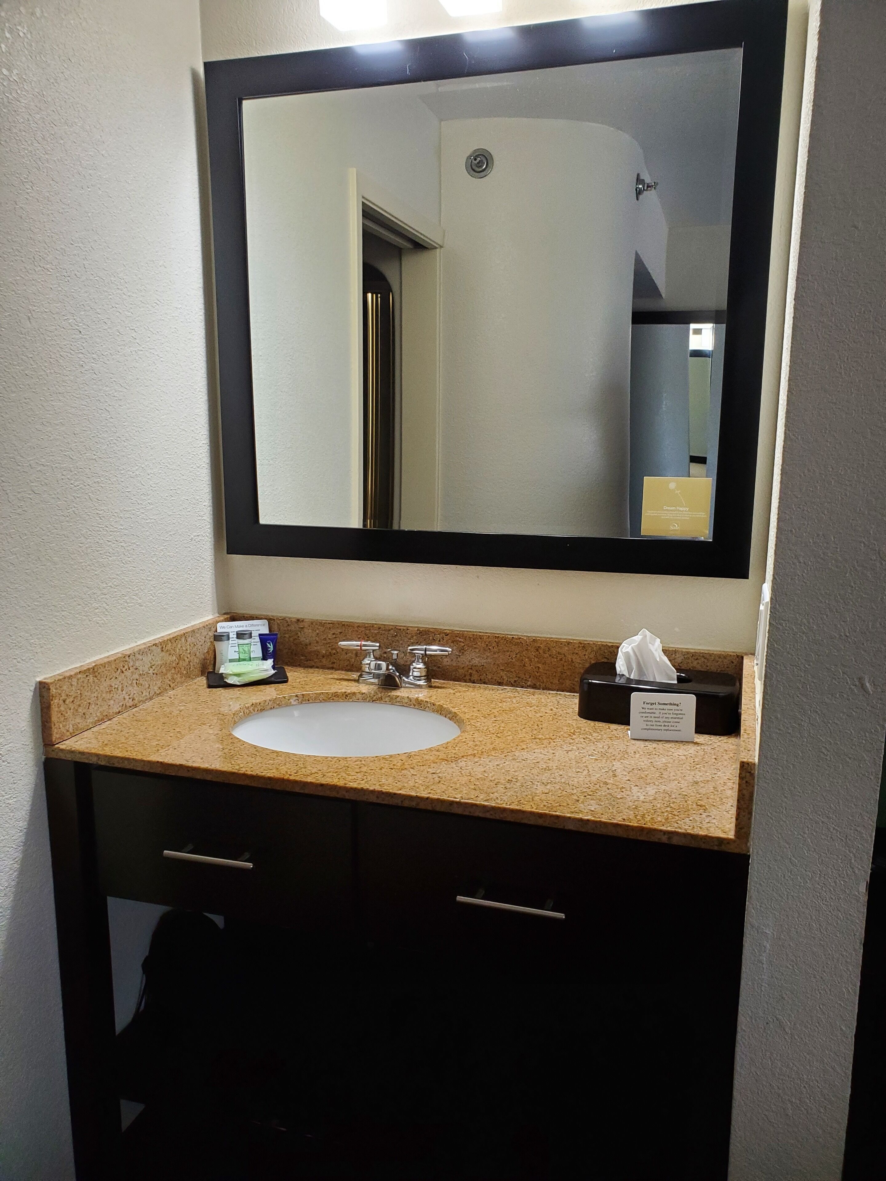 Un baño con un lavamanos, dos grifos, un espejo y una caja de pañuelos.