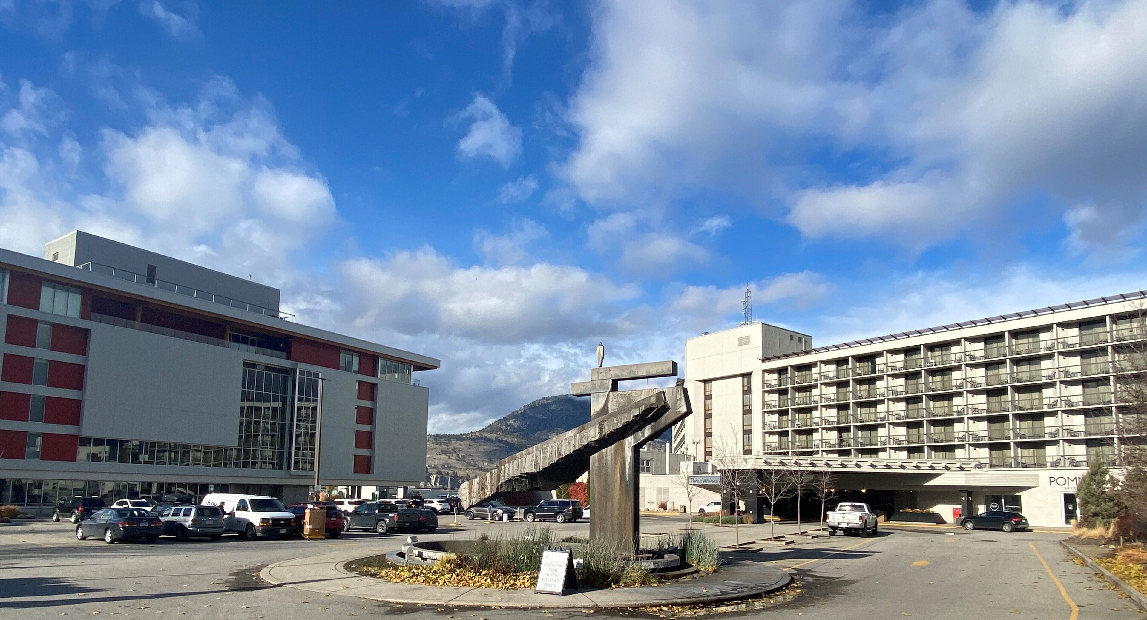 A parking lot with several cars, a large building with multiple floors, and a mountain in the background.