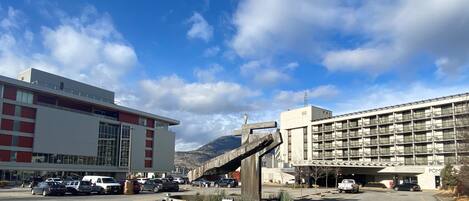 A parking lot with several cars, a large building with multiple floors, and a mountain in the background.