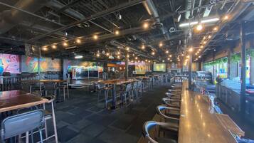 A spacious indoor dining area with high ceilings, exposed ductwork, and a variety of seating options including bar stools and tables.