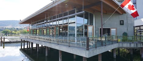 Un edificio frente al agua con fachada de vidrio, una bandera canadiense y un muelle que se adentra en el agua.