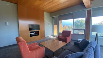 Un salon moderne avec un plafond en bois, un téléviseur à écran plat fixé au mur, un canapé, un fauteuil rouge et une table basse.