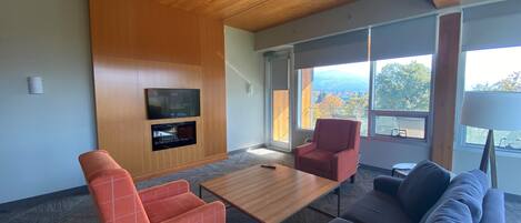 A modern living room with a wooden ceiling, a flat-screen TV mounted on the wall, a sofa, a red armchair, and a coffee table.