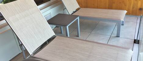 A room with two reclining chairs with fabric seats and metal frames, a wooden wall, and a window with blinds.