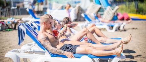 A beach with lounge chairs and people relaxing.