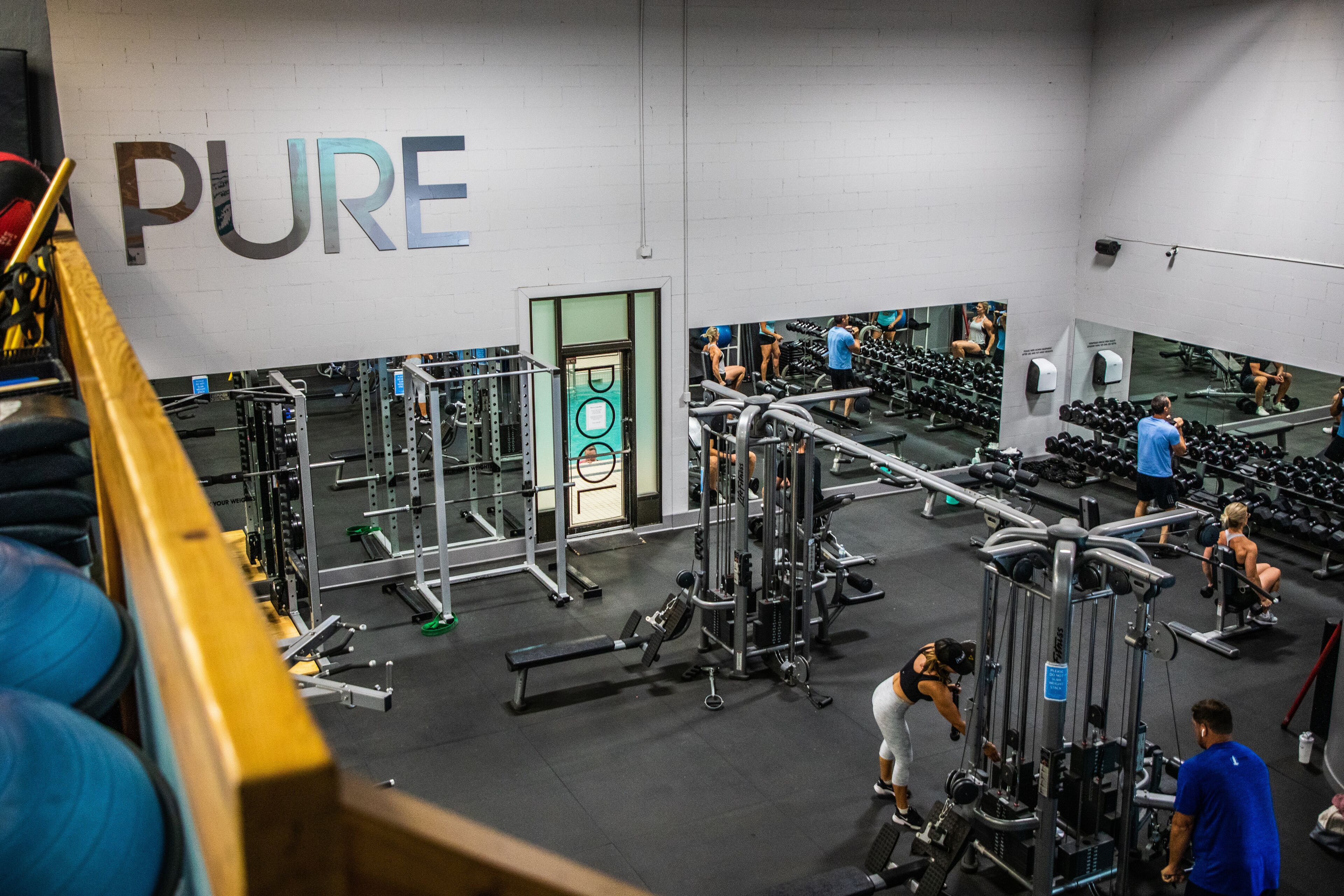 A gym with various exercise equipment, a mirrored wall, and a sign that reads "PURE".