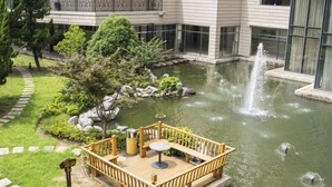 A wooden deck with a table and chairs, a small pond with a fountain, and a stone pathway.