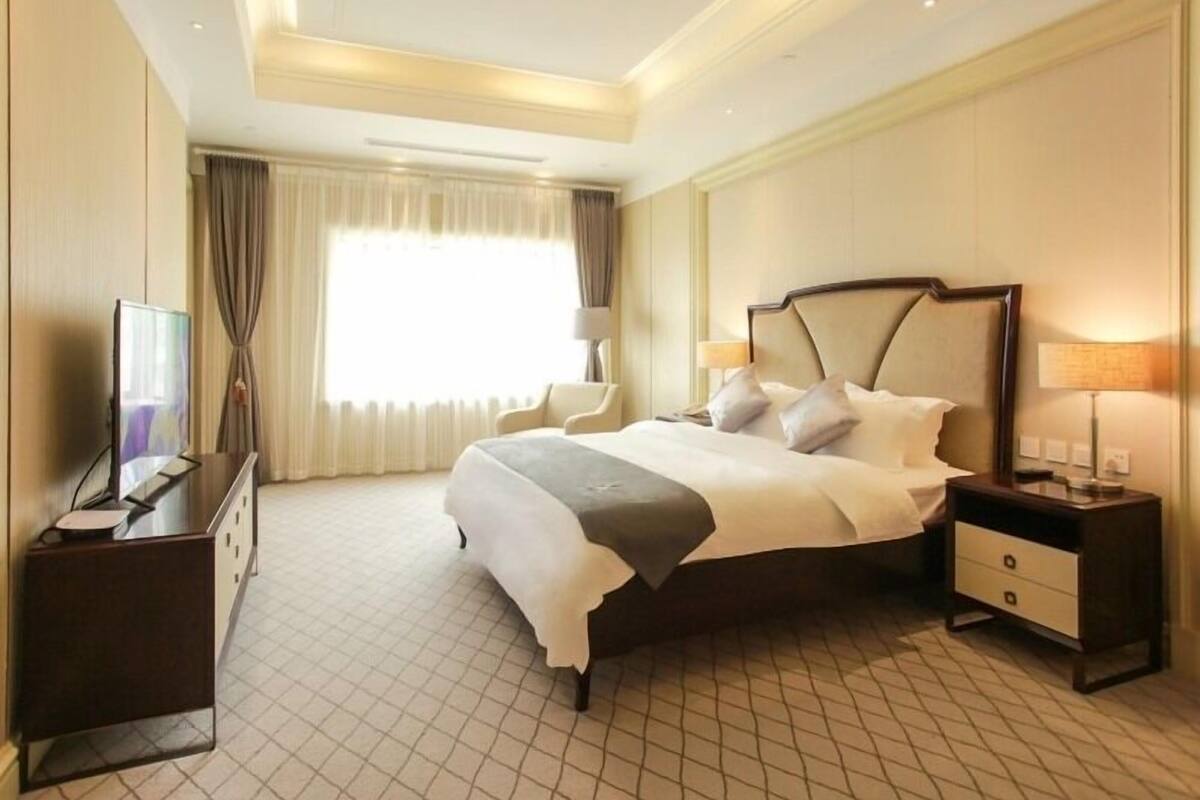 A hotel room with a large bed, bedside tables, a desk, and a television.