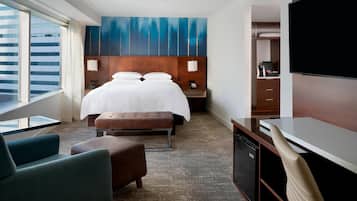 Habitación de hotel con una cama grande, un escritorio, una televisión y vistas de la ciudad.