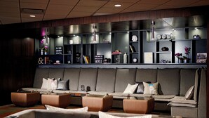 A modern hotel lobby with a seating area featuring leather sofas and armchairs, a reception desk, and a wall with shelves displaying various items.