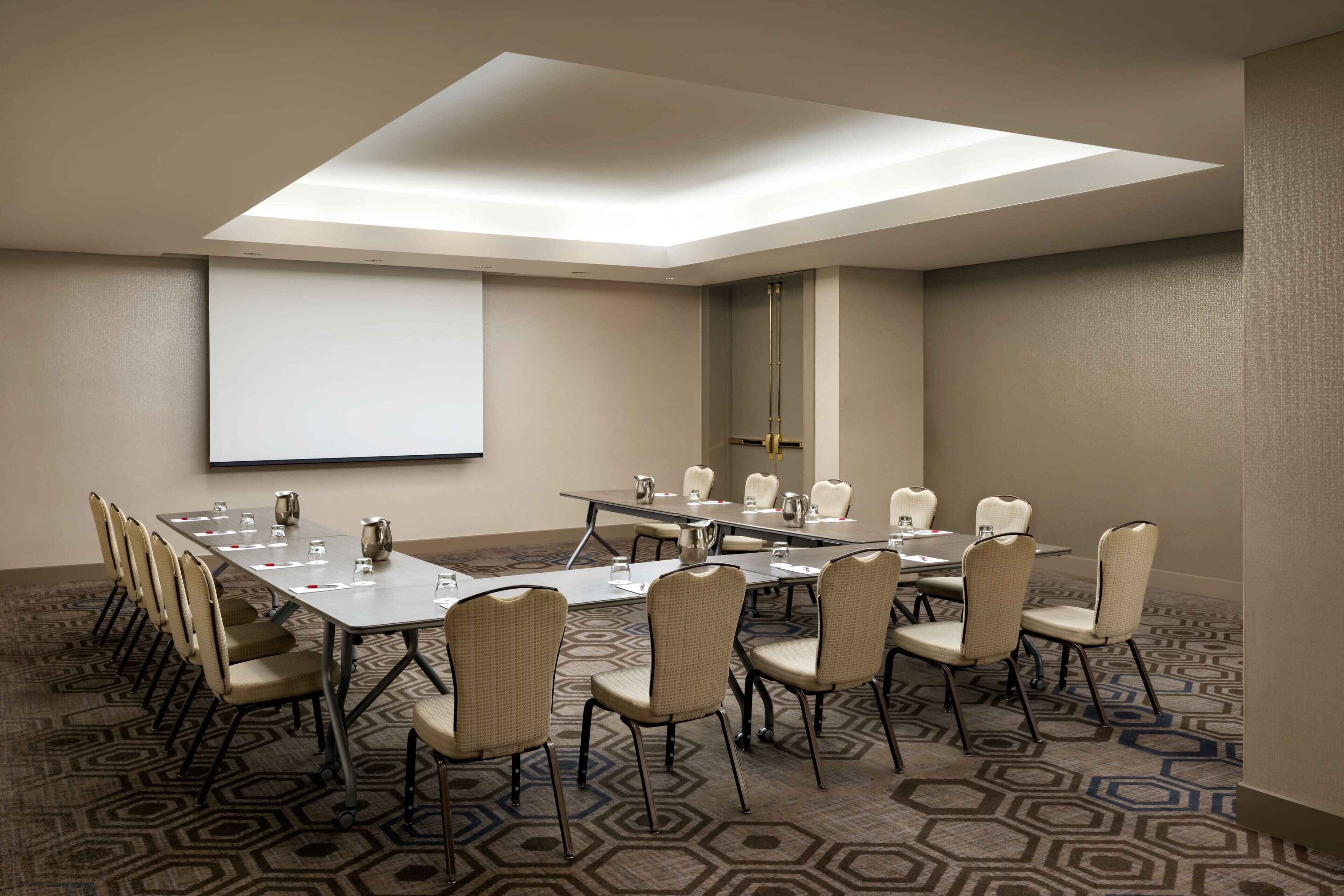 A conference room with a large table, chairs, a projector screen, and a patterned carpet.