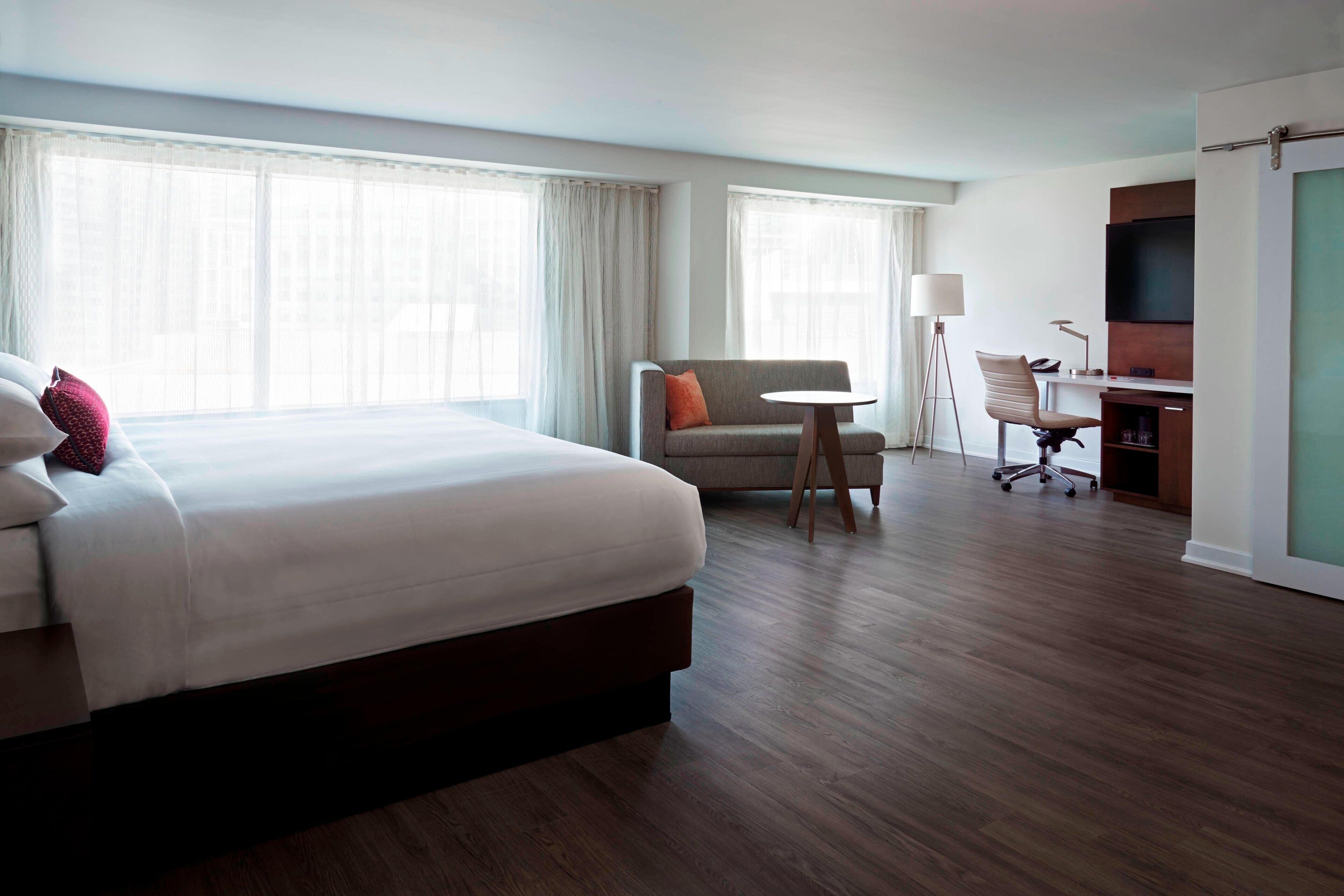A hotel room with a large bed, a desk with a chair, a small table, and a TV.
