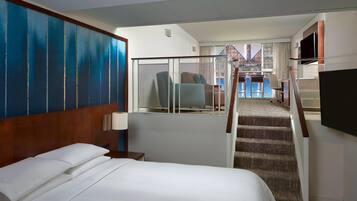 Een hotelkamer met een groot bed, een televisie, een trap en uitzicht op het zwembad.