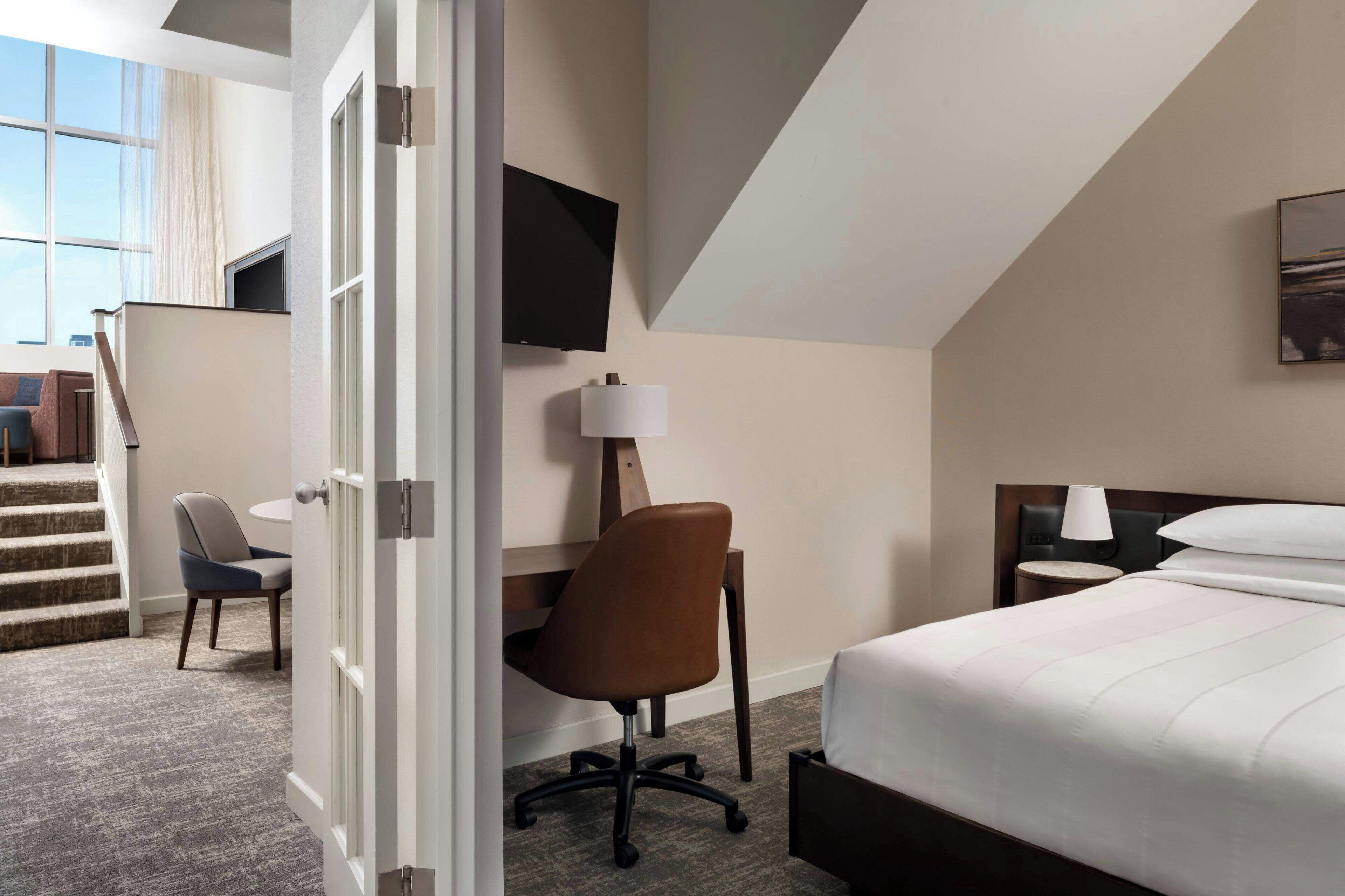 Une chambre d’hôtel équipée d’un lit, d’un bureau, d’une chaise, d’une télévision et d’un escalier menant à une autre pièce.