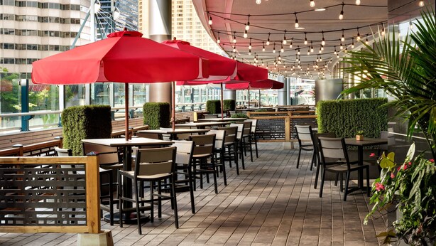 An outdoor café with tables and chairs, red umbrellas, and greenery.
