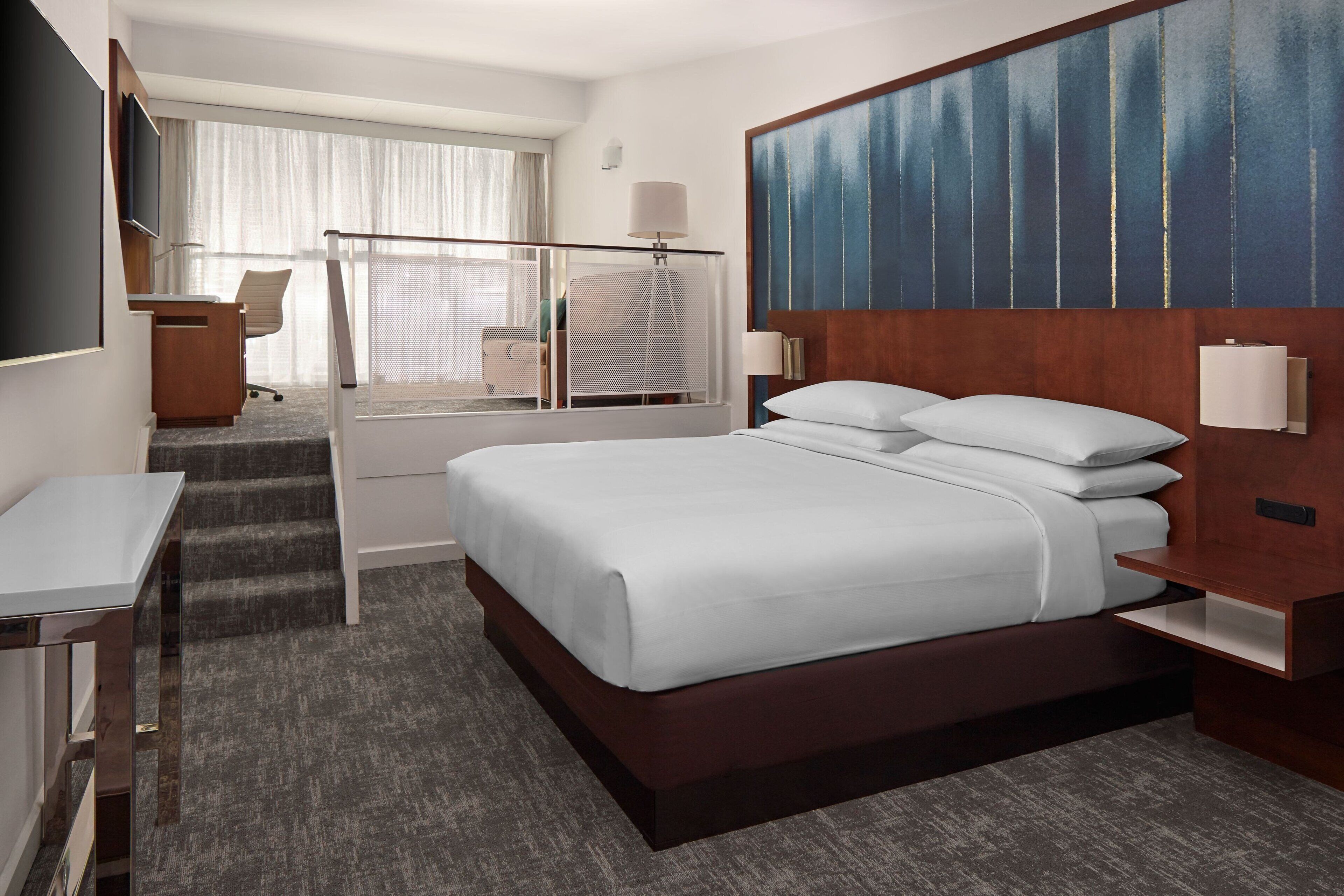 Habitación de hotel con una cama grande, un escritorio, una silla, un televisor y una ventana con cortinas.