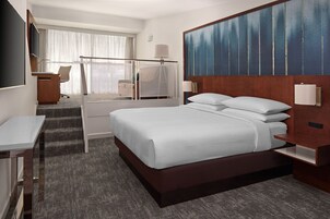 Een hotelkamer met een groot bed, een bureau, een stoel, een televisie en een raam met gordijnen.